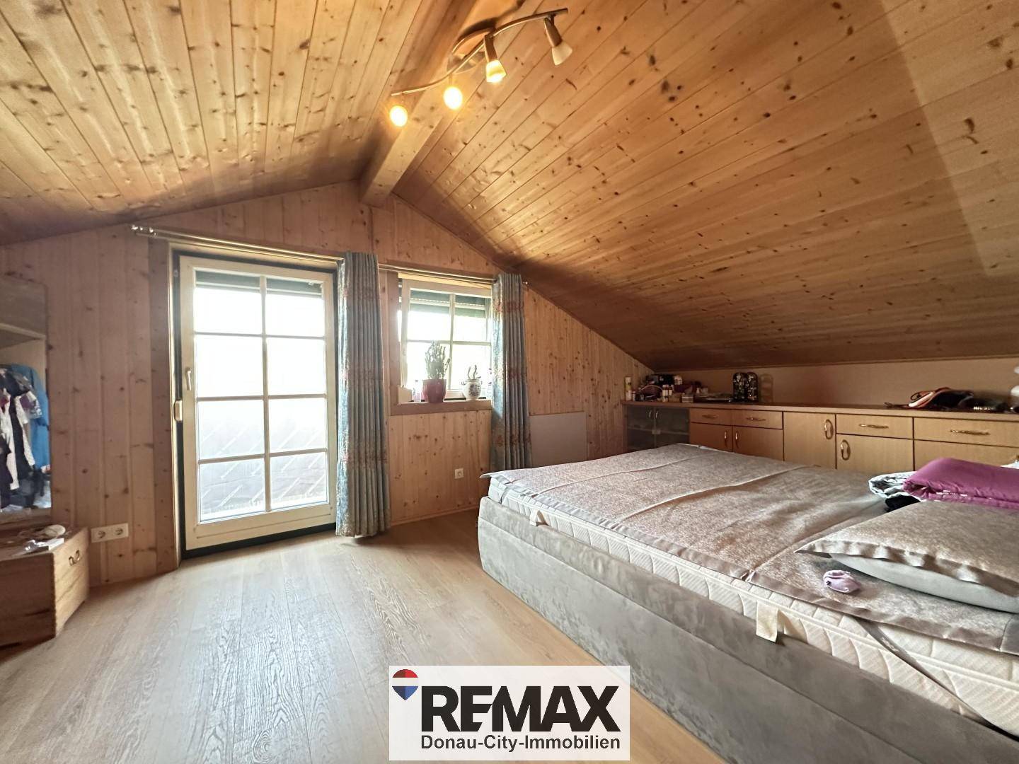 Gemütliches Schlafzimmer mit Holztäfelung, Dachschräge und Zugang zu einem Balkon.
