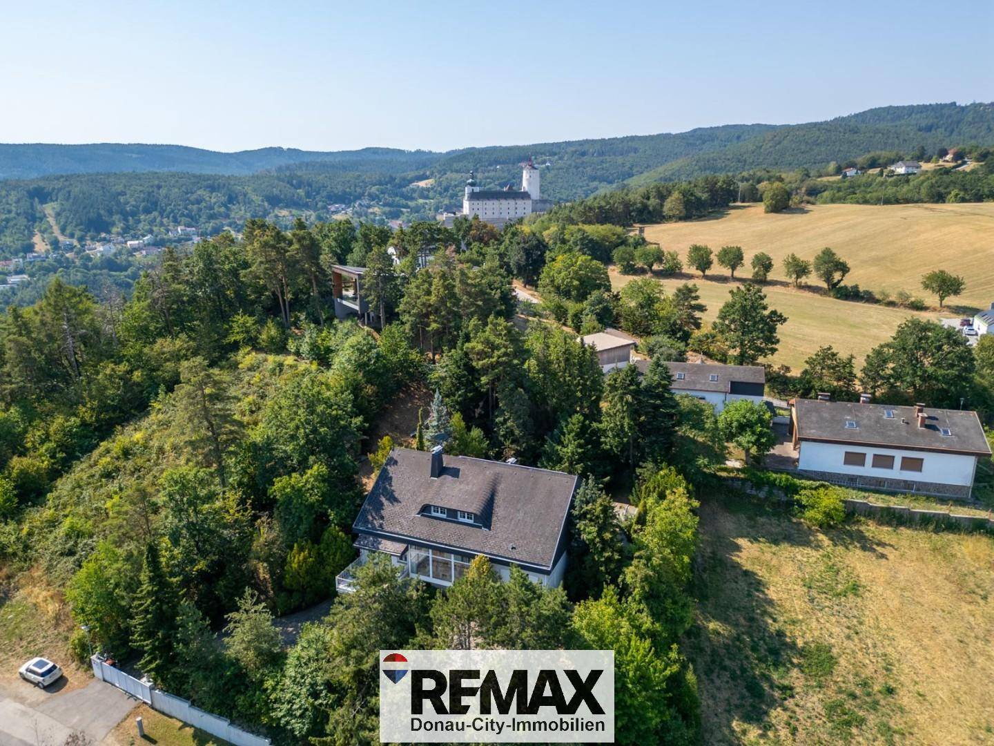 Weitläufige Luftaufnahme des Anwesens in hügeliger Landschaft mit Wald und einem Schloss in der Ferne.