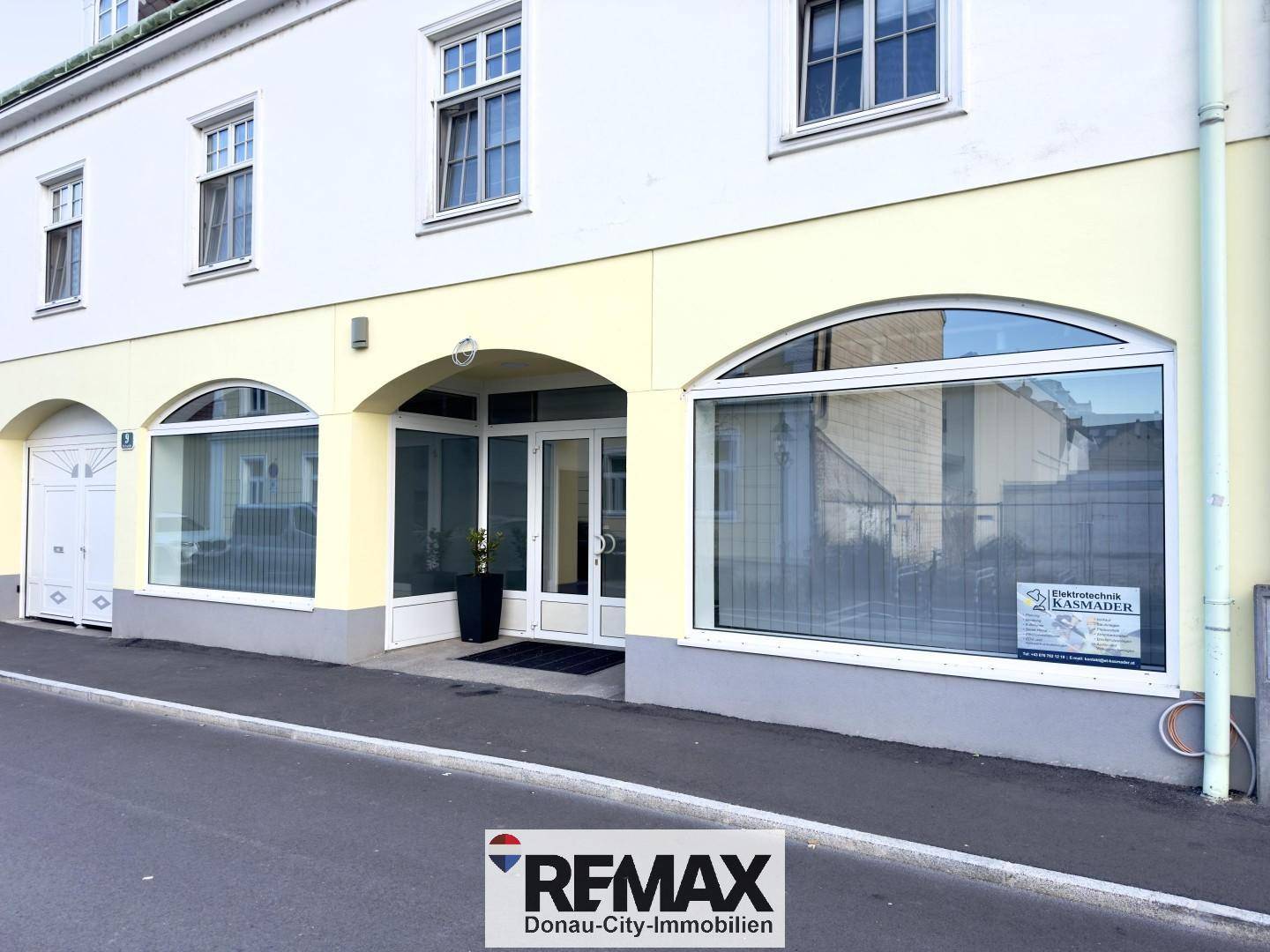Fassade eines Geschäftsgebäudes mit großen Bogenfenstern und einem überdachten Eingangsbereich an der Straße.