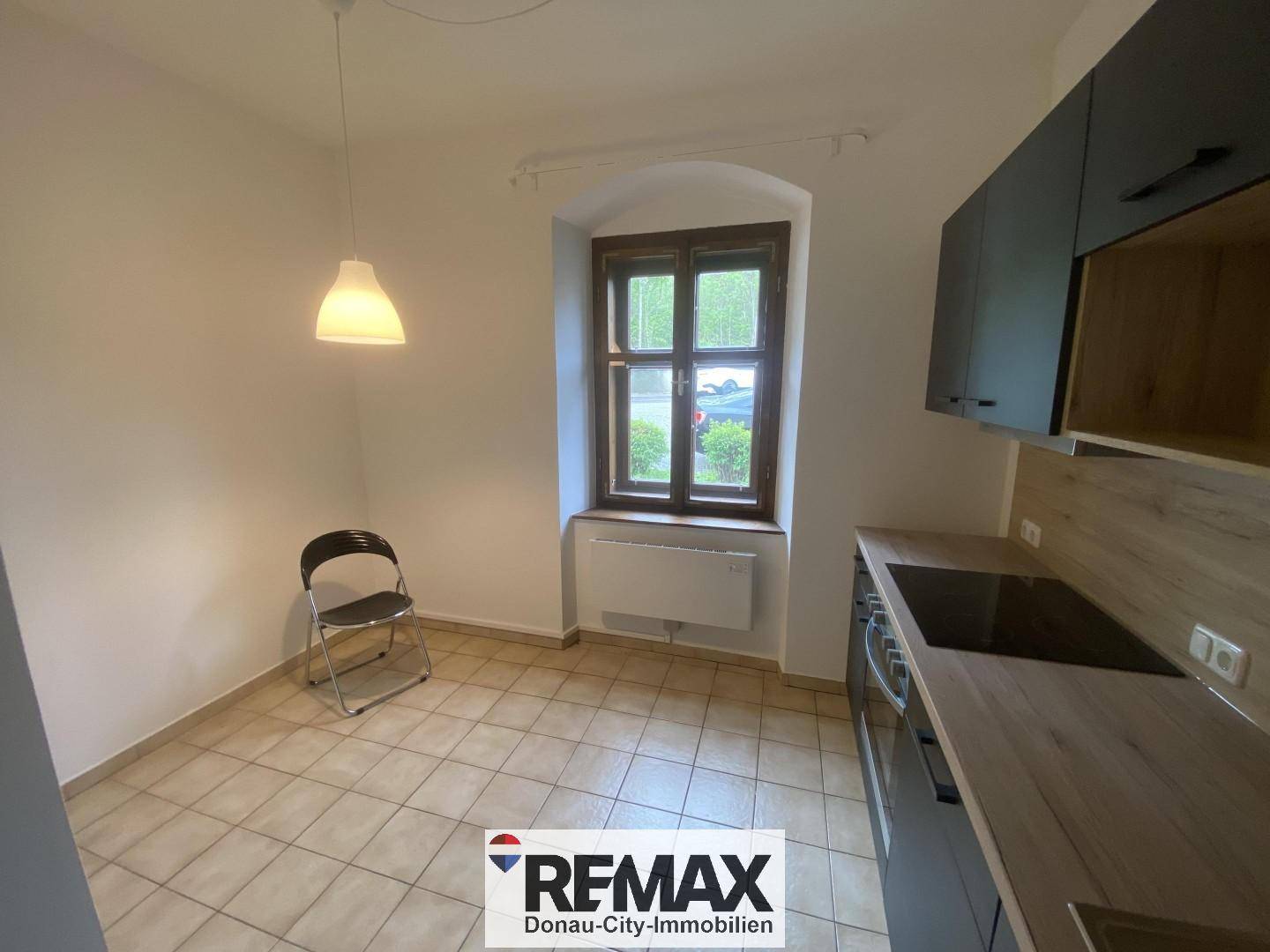Kleine Küche mit Fliesenboden, Fenster und moderner Küchenzeile in dunklem Design.