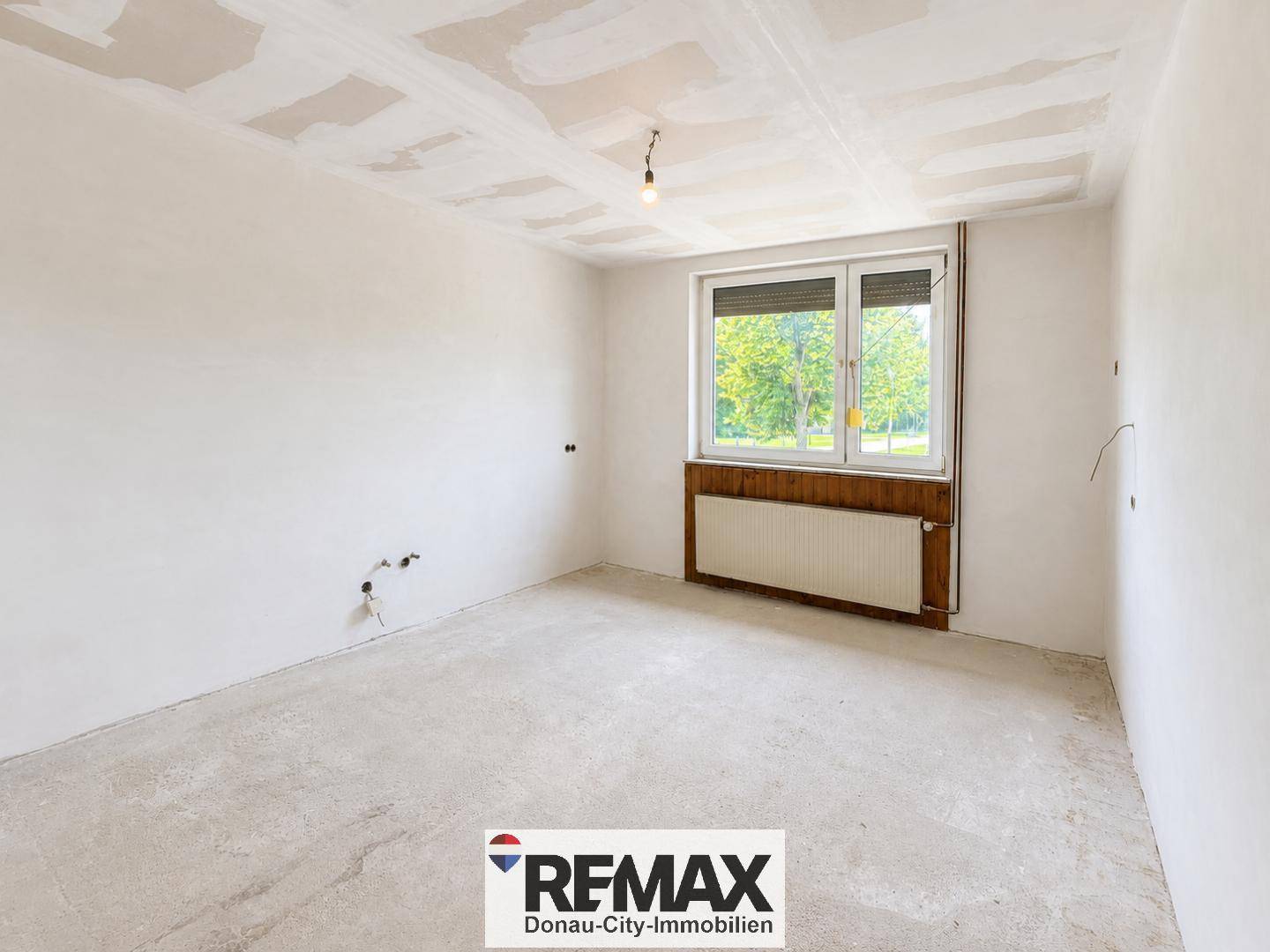 Raum in Renovierung mit großem Fenster, Heizkörper und unfertigem Boden.