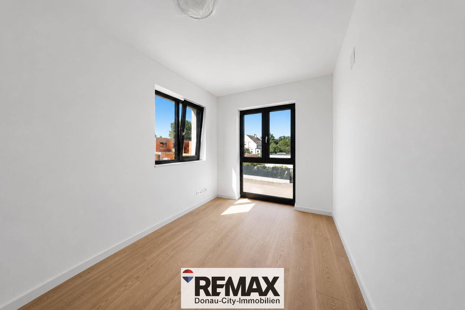 Helles, leeres Zimmer mit Holzboden und Fenster mit Zugang zu einem französischen Balkon.