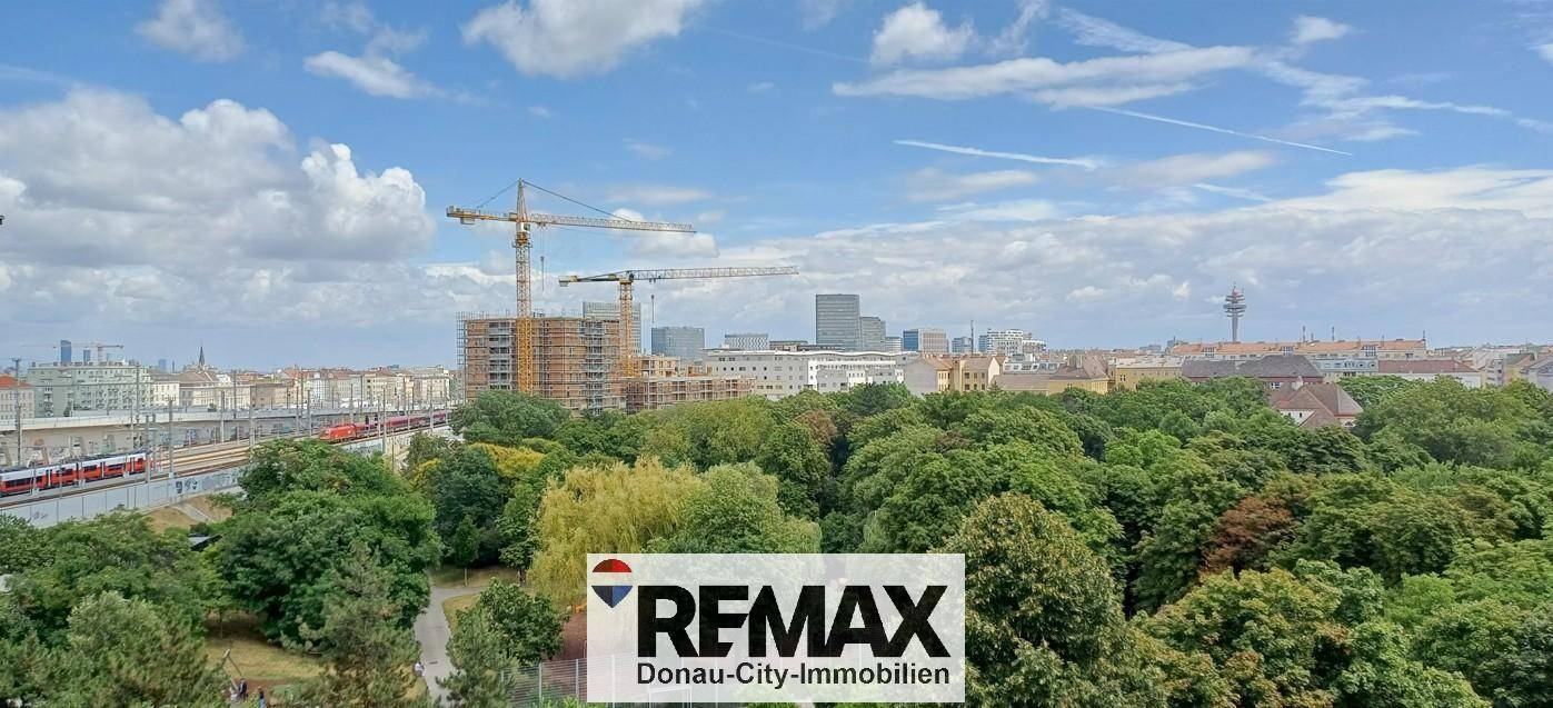 Weitläufiger Blick über die Stadt mit viel Grün, Bahngleisen und neuen Bauprojekten.