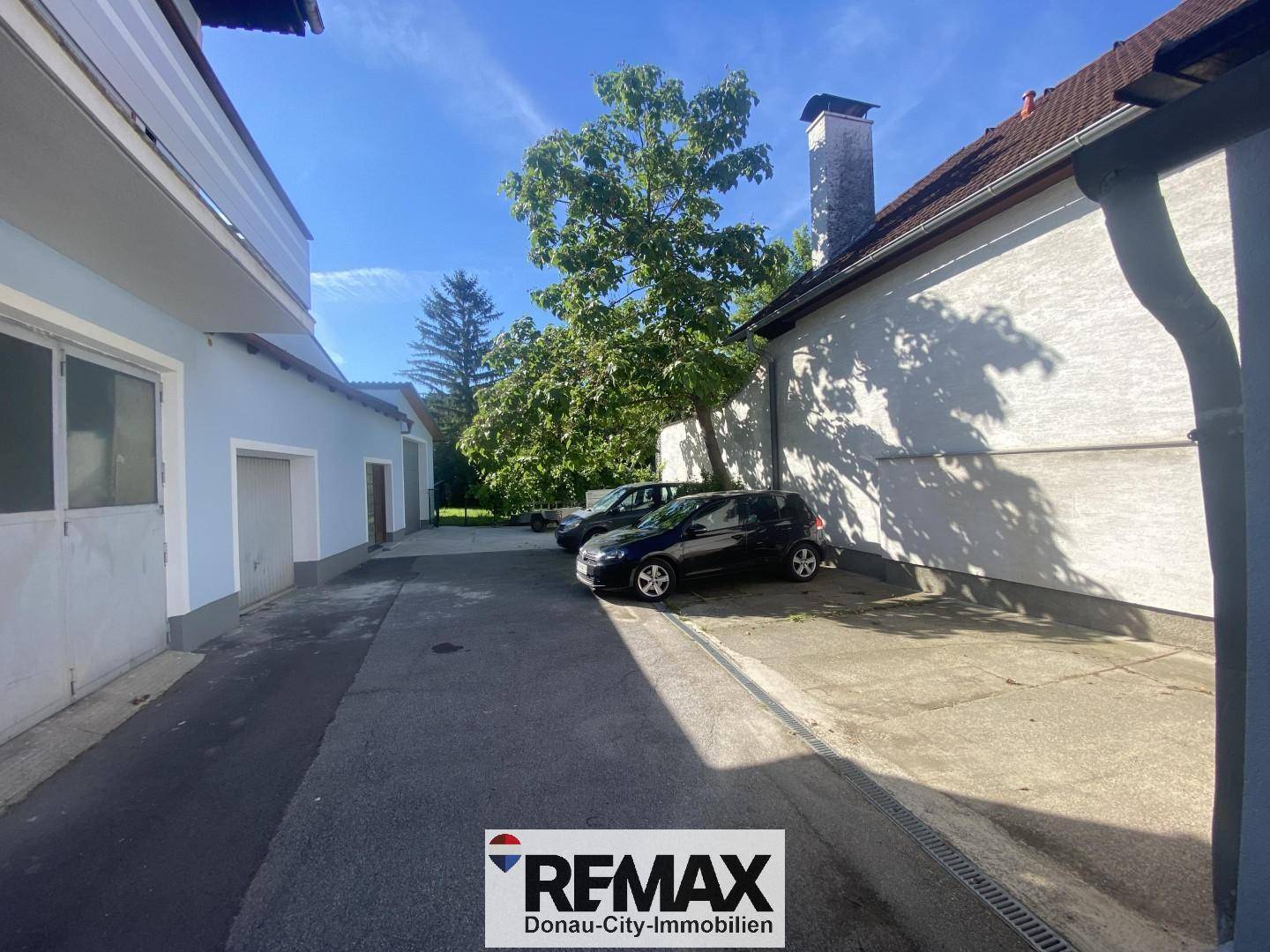 Außenbereich mit gepflastertem Hof, Parkplätzen und Garagenzufahrten zwischen Gebäuden.