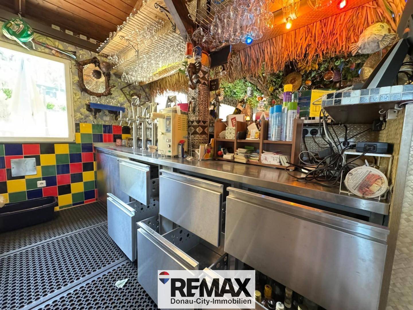 Arbeitsbereich hinter der Bar mit Edelstahloberflächen, Zapfanlagen und farbenfrohen Fliesen an der Wand.