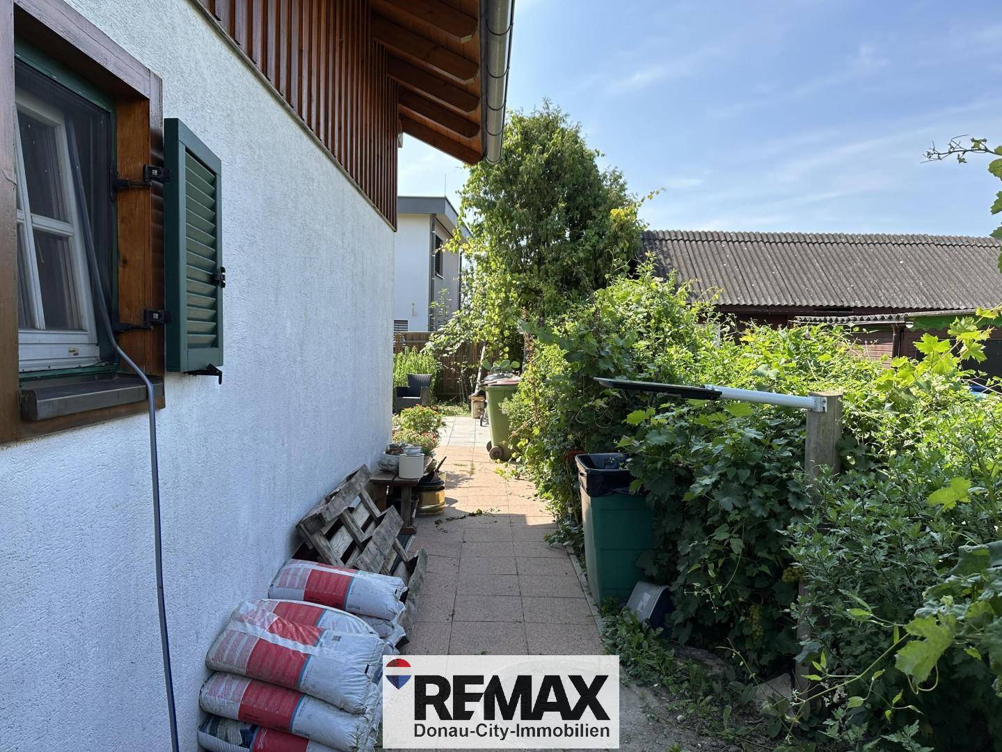 Seitenweg des Hauses mit üppigem Grün und praktischen Lagerbereichen.