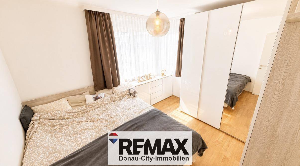 Helles Schlafzimmer mit Doppelbett, Spiegelschrank und Holzfußboden.