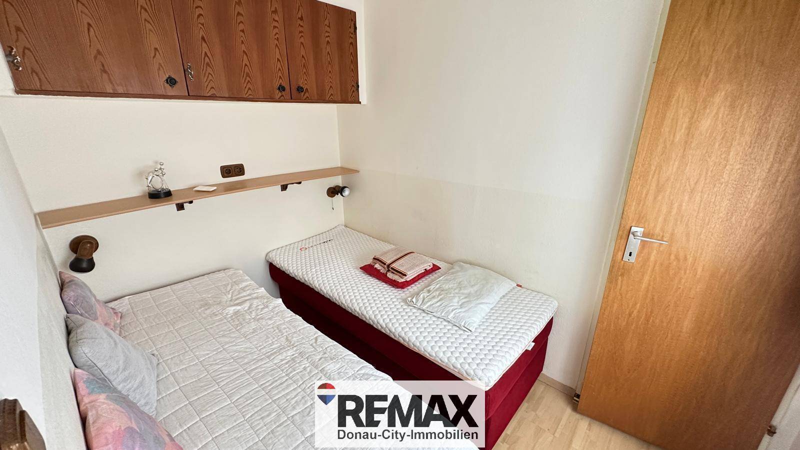 Kleines Schlafzimmer mit zwei Einzelbetten und praktischen Holzschränken über den Betten.