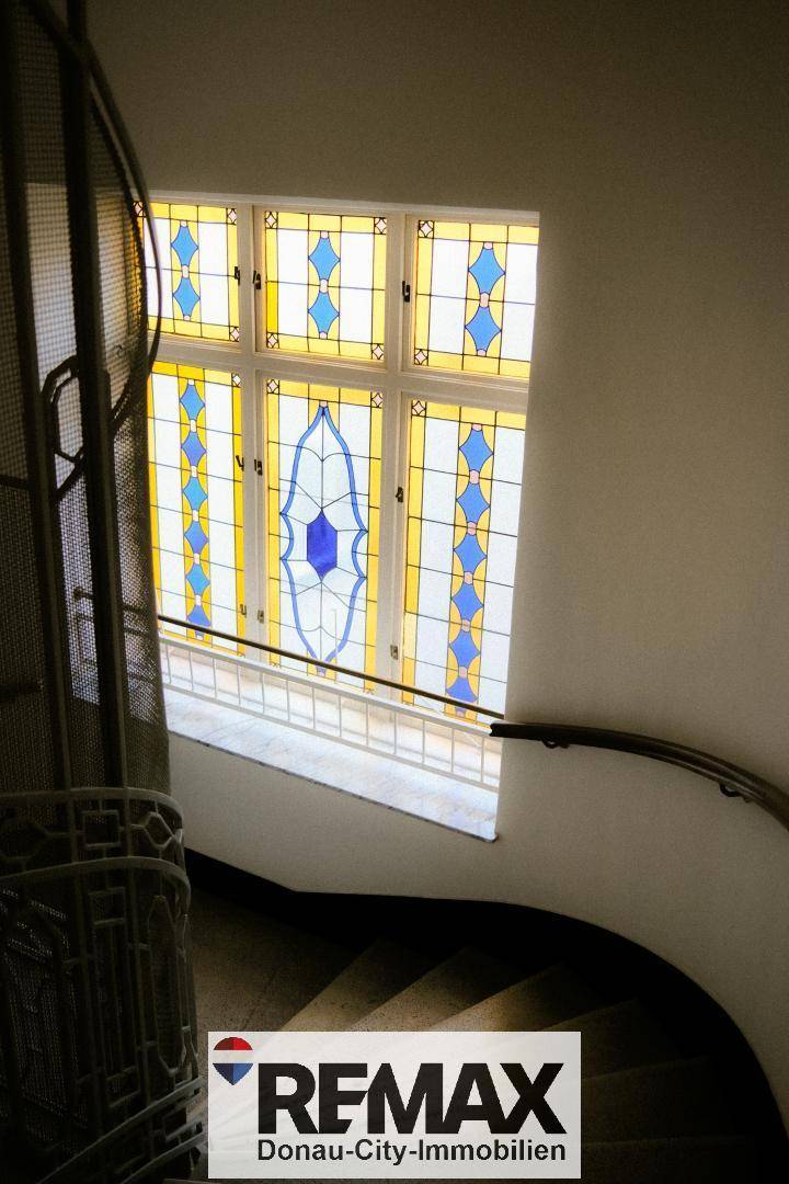 Historisches Treppenhaus mit kunstvollen Buntglasfenstern und schmiedeeisernem Geländer.