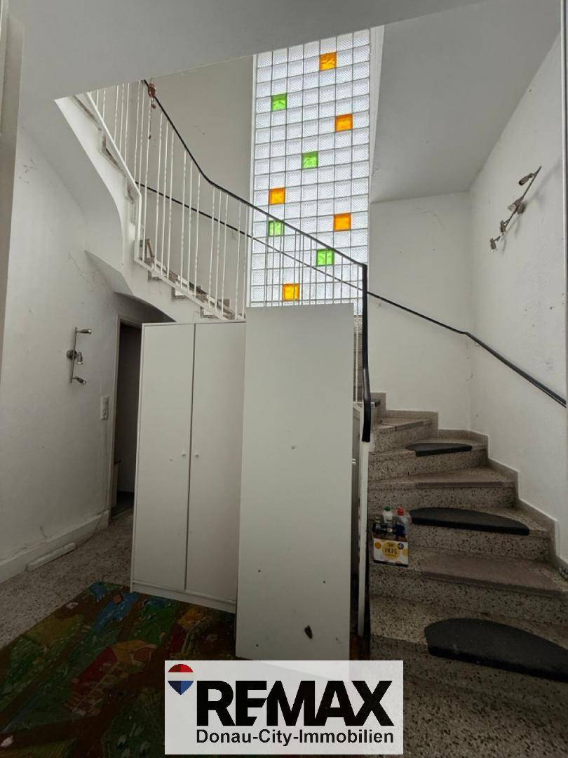 Treppenhaus mit Terrazzoboden und einem farbigen Glasbausteinfenster, das Licht spendet.