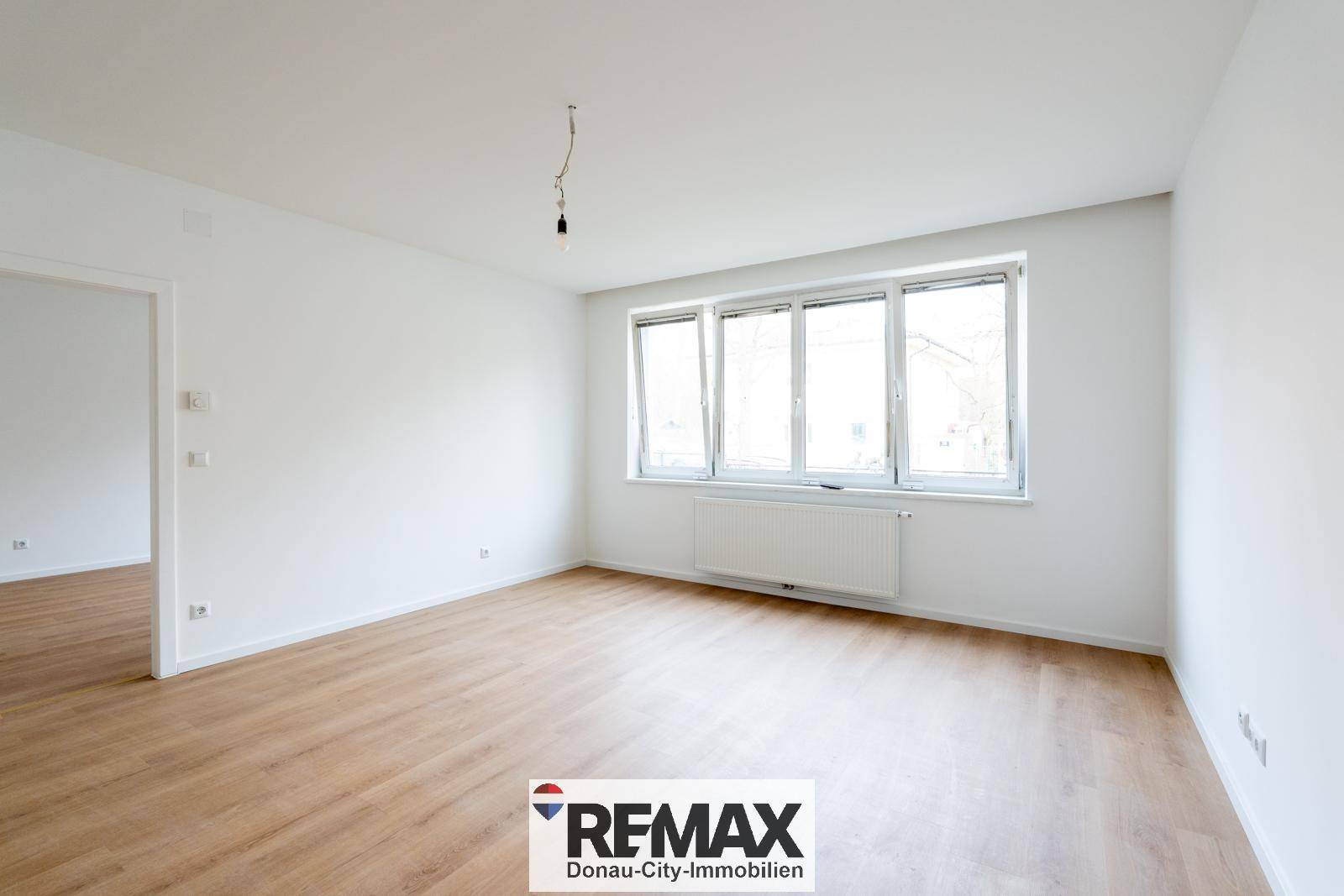 Lichtdurchfluteter Raum mit großem Fenster, Heizkörper und hellem Laminatboden.
