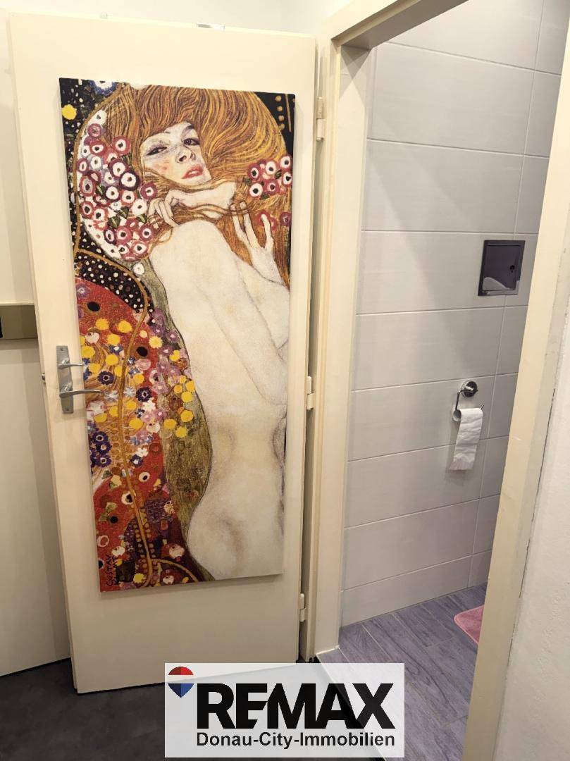 Tür mit dekorativem Gemälde, die zu einem modern gefliesten Badezimmer führt.