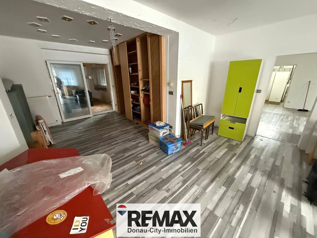 Geräumiger Wohnbereich mit modernem Laminatboden und eingebauten Regalen, teilweise renovierungsbedürftig.