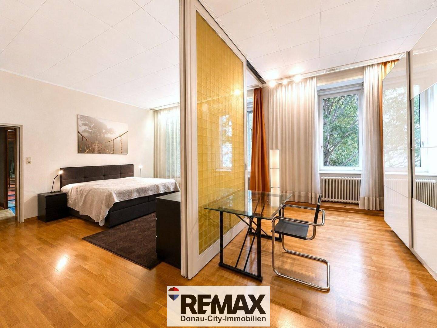 Schlafzimmer mit Doppelbett, Nachttischen und einem kleinen Arbeitsbereich mit Glastisch.