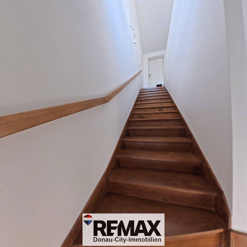 Holztreppe mit hellem Geländer, die in die obere Etage des Hauses führt.