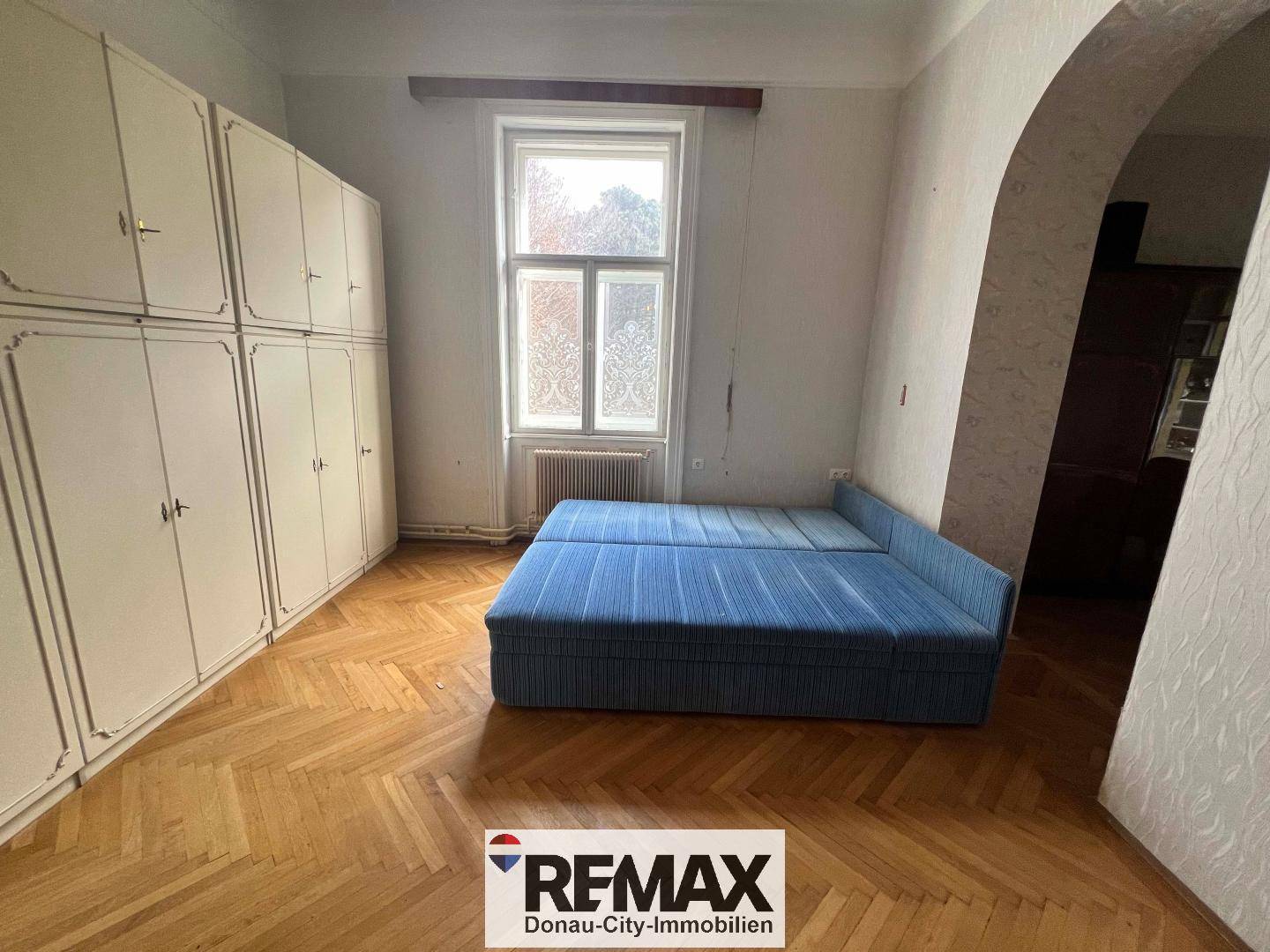 Schlafzimmer mit Fischgrätparkett, Einbauschränken und einem blauen Sofa.