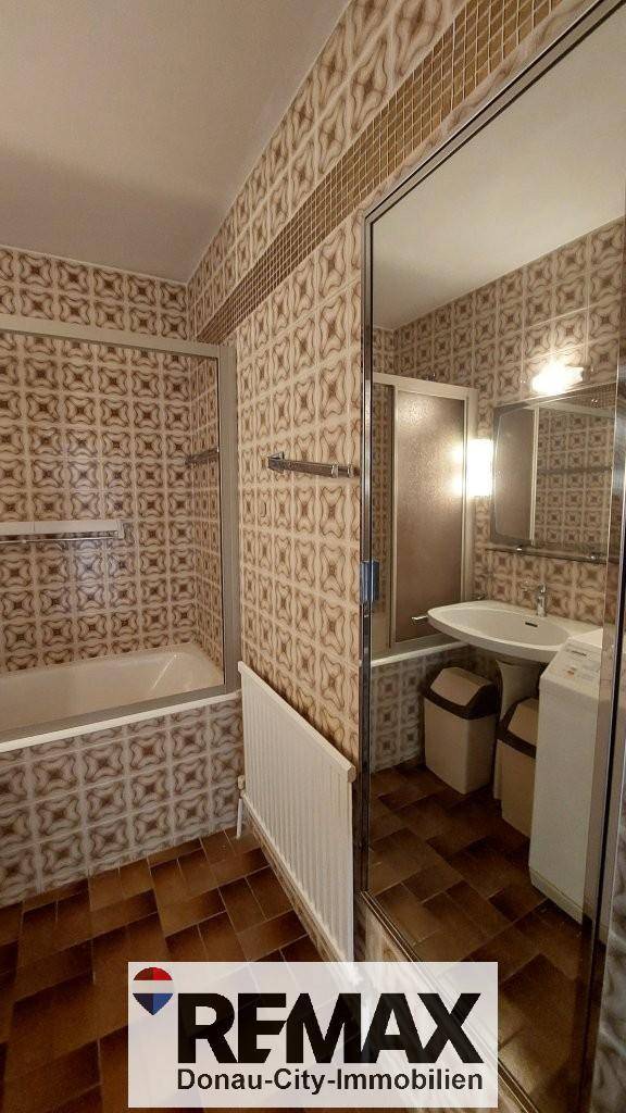 Badezimmer mit gemusterten Fliesen, Badewanne mit Duschabtrennung und großem Spiegel.