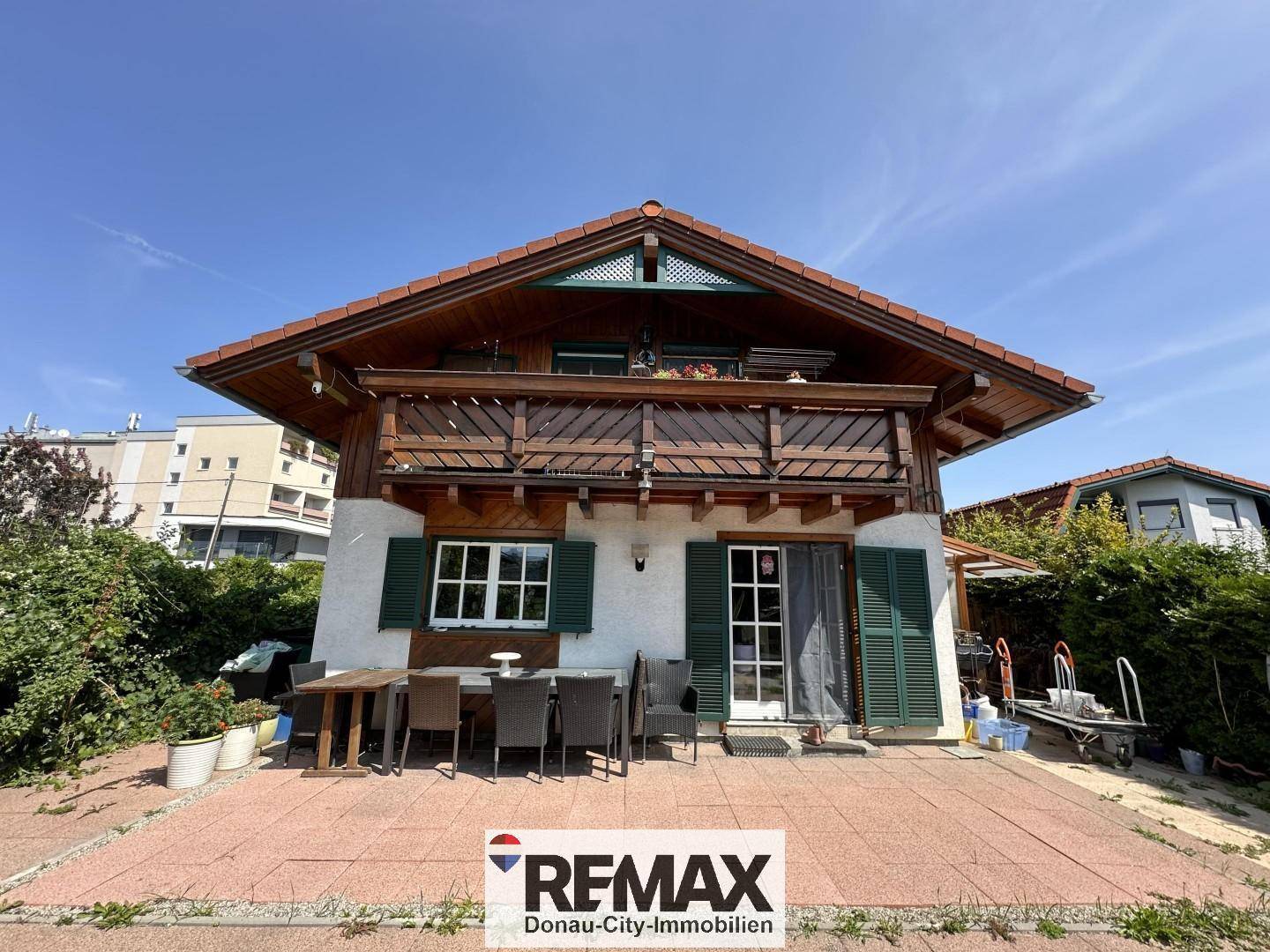 Rückansicht des Hauses mit großer gepflasterter Terrasse und Gartenmöbeln.