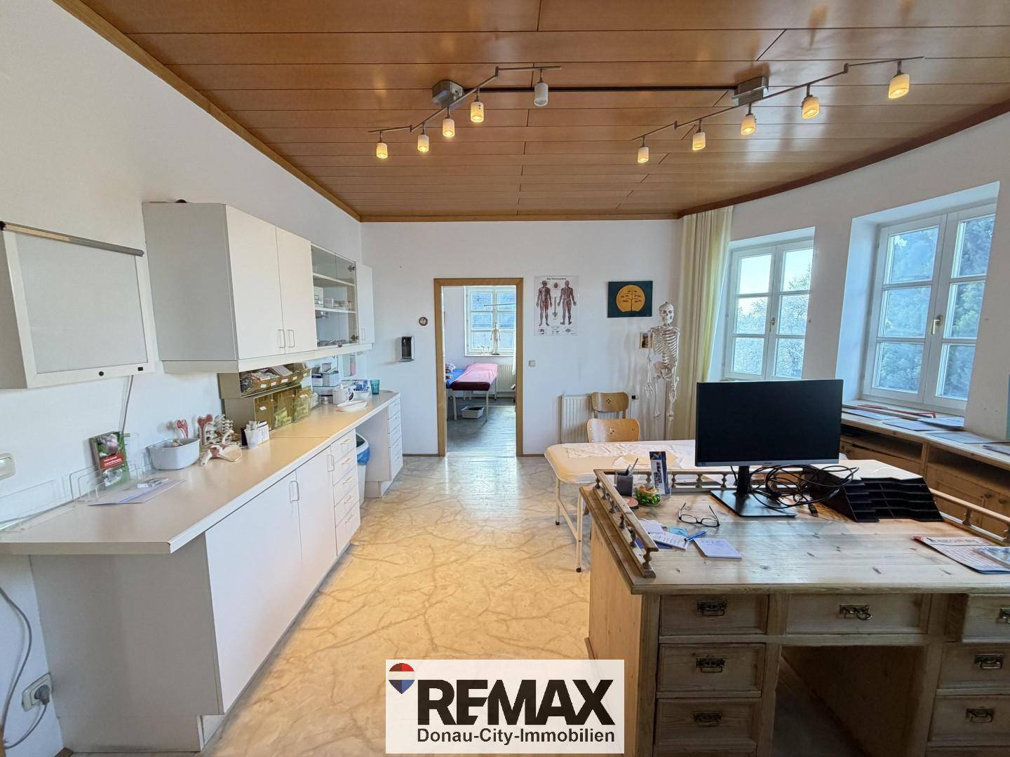Behandlungszimmer oder Büro mit Schreibtisch, medizinischen Schränken und Holzdecke.