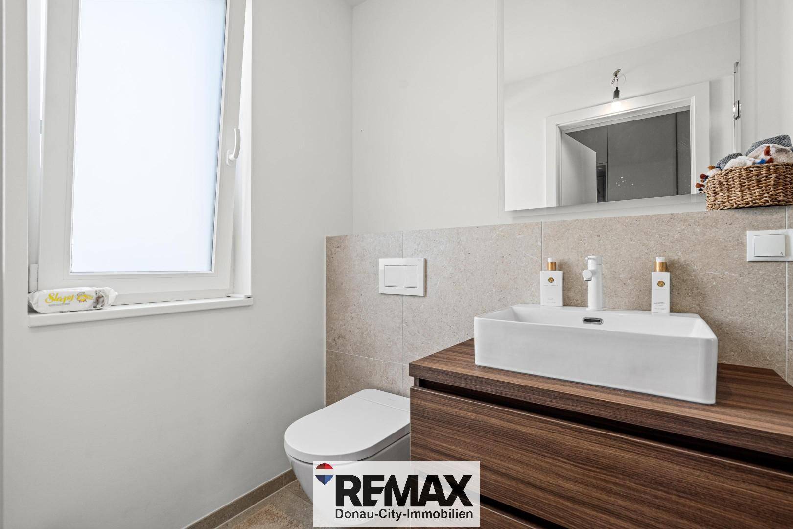 Modernes Badezimmer mit Waschtisch, wandhängendem WC und Fenster für Tageslicht.