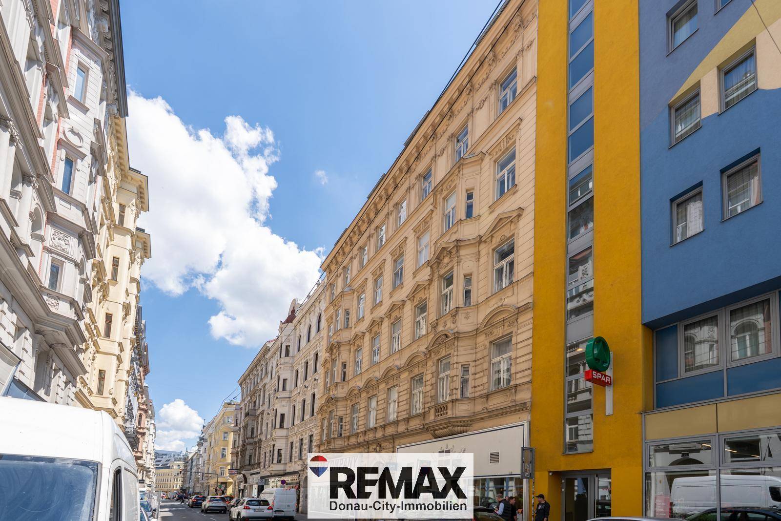 Historische und moderne Gebäude entlang einer belebten Straße unter blauem Himmel.