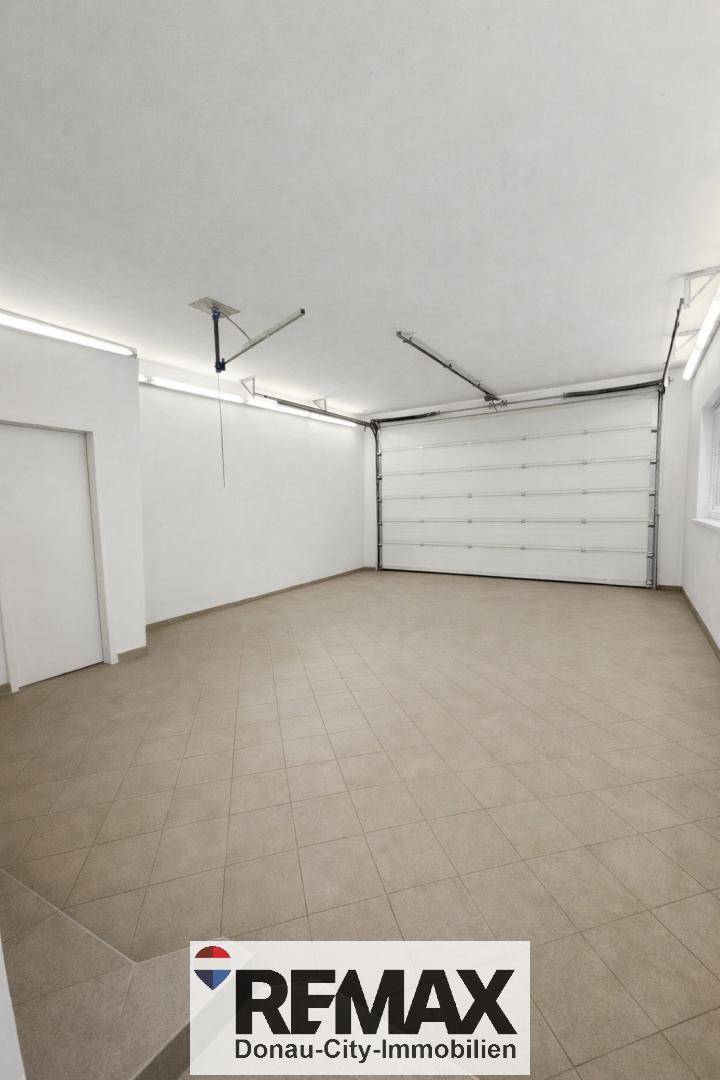 Weitere Ansicht der leeren Garage mit Fliesenboden, Garagentor und einem Fenster.