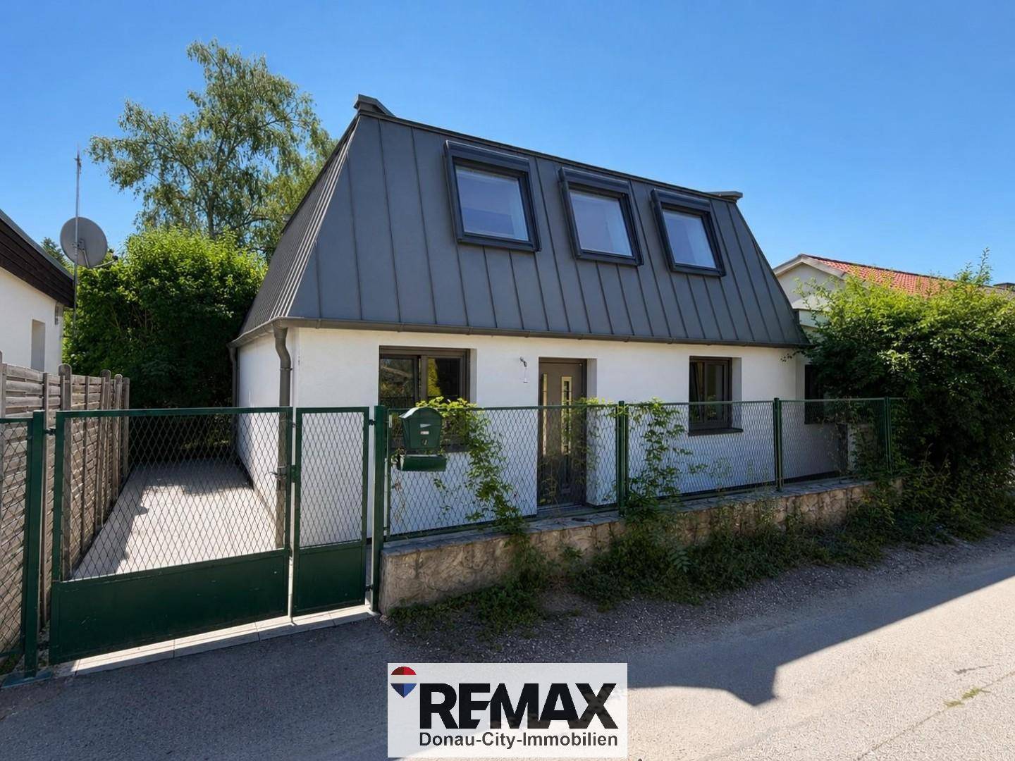 Vorderansicht eines Hauses mit Mansarddach, Dachfenstern und einem umzäunten Vorgarten.