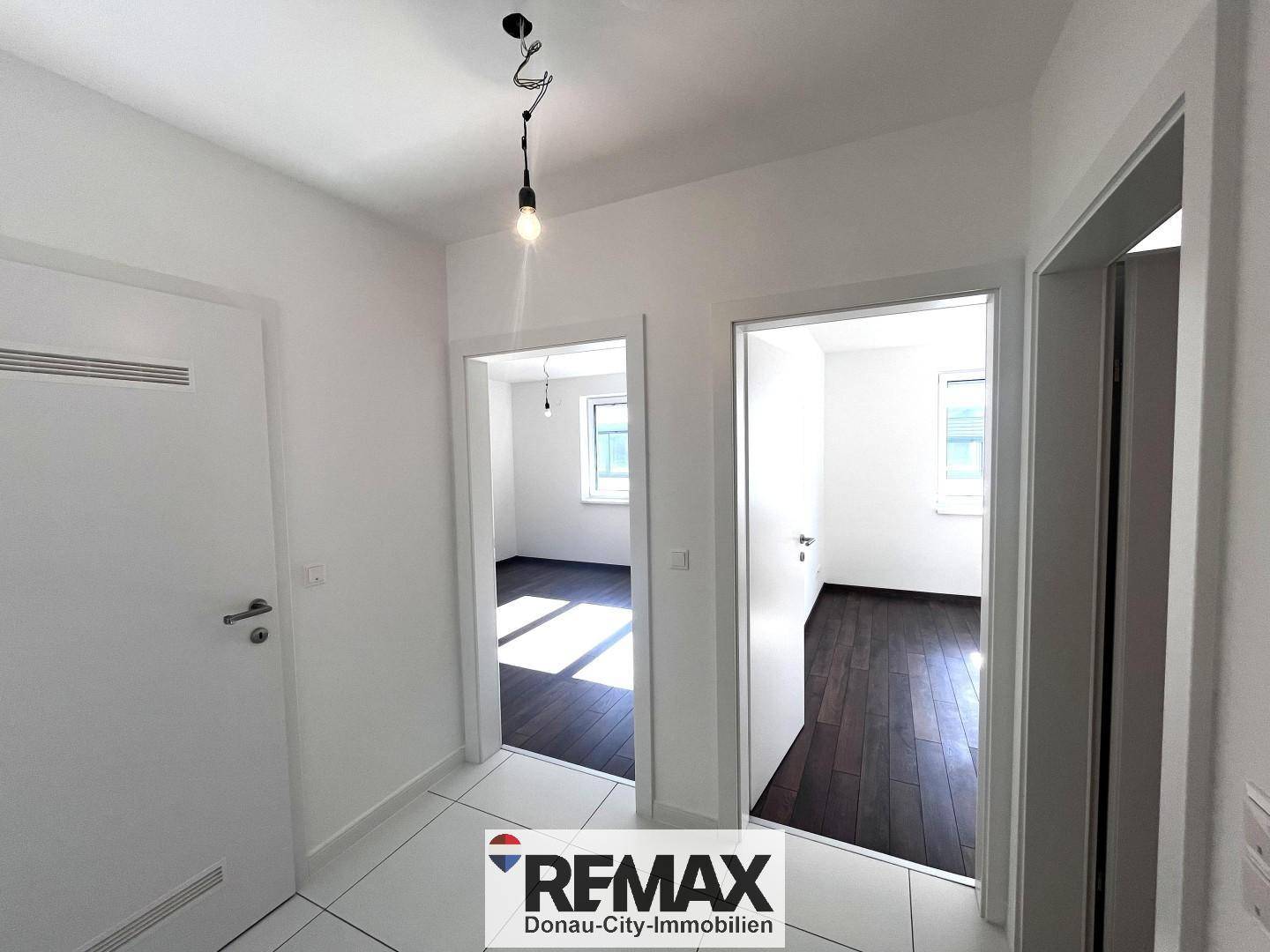 Flur mit weißen Fliesen und Zugang zu mehreren hellen Zimmern mit Holzboden.