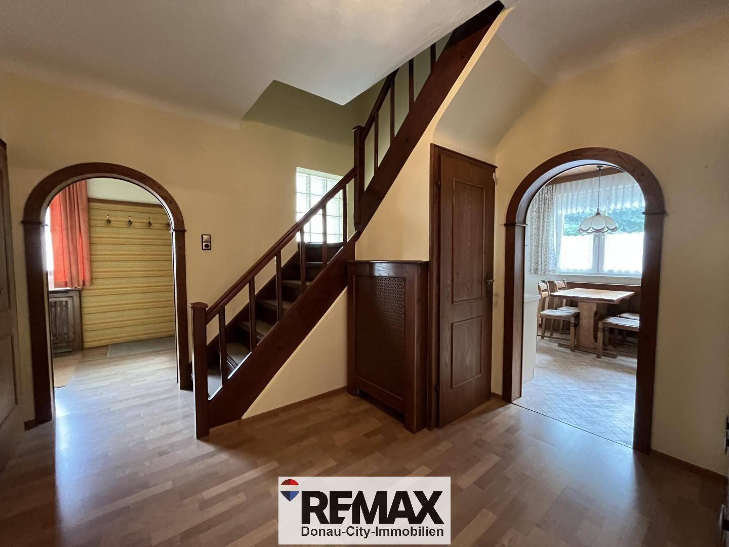 Heller Flur mit Holztreppe, Holzboden und traditionellen Rundbögen zu den angrenzenden Räumen.