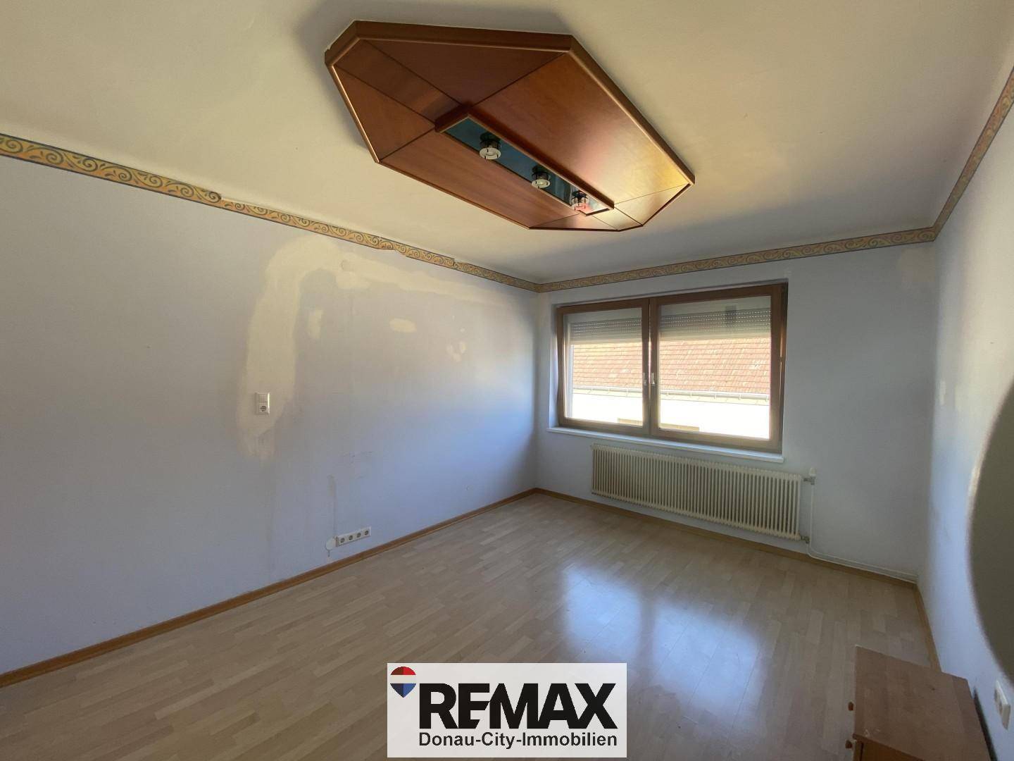 Helles Wohnzimmer mit Laminatboden, Fenster mit Rollläden und dekorativer Deckenverkleidung.