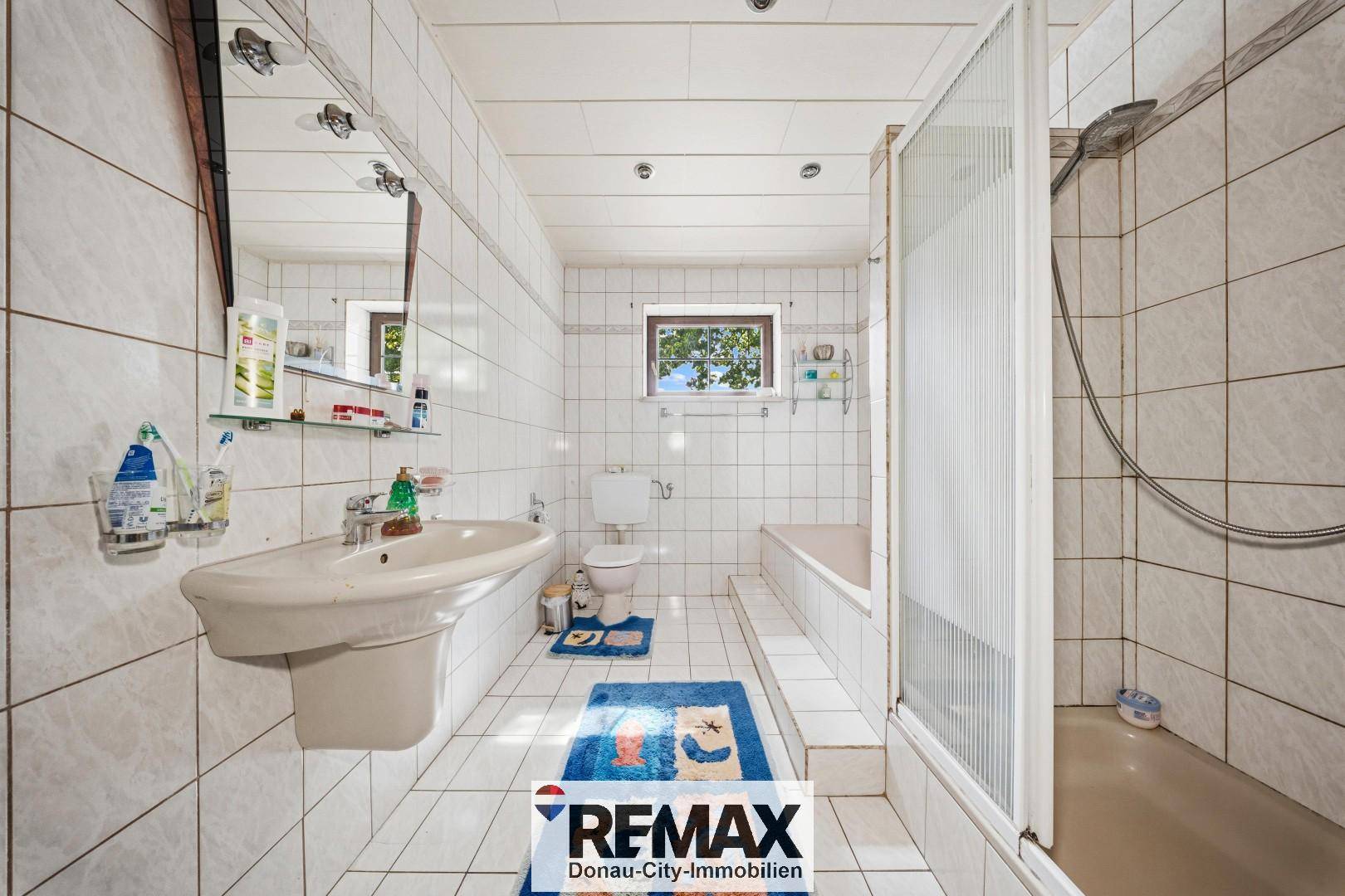 Gefliestes Badezimmer mit Dusche, Badewanne, Waschbecken und Fenster, in hellem Design.