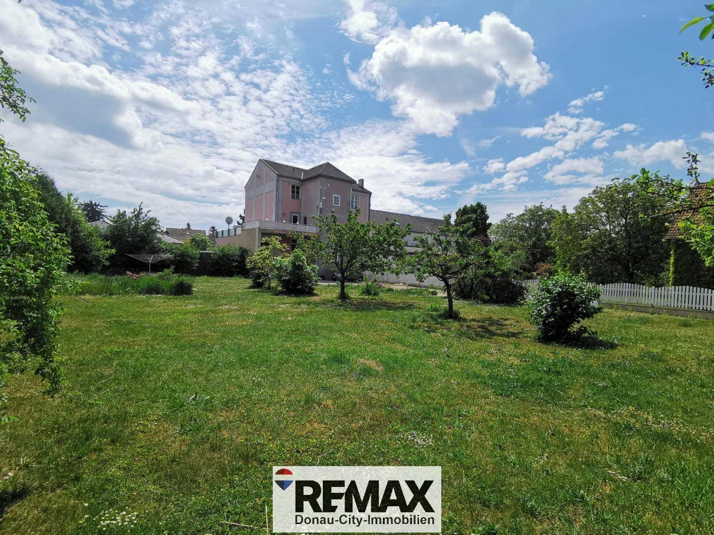 Großer Gartenbereich mit Rasenfläche, Bäumen und dem Hauptgebäude im Hintergrund.