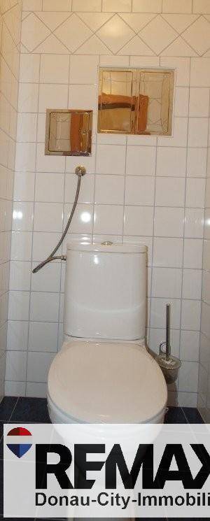 Separate Toilette mit weißen Wandfliesen und dunklem Boden, funktional und sauber.