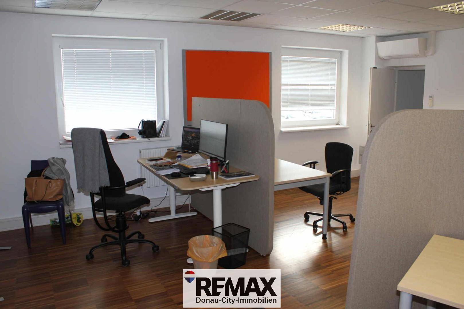 Offenes Büro mit getrennten Arbeitsbereichen, orangefarbener Akzentwand und Klimaanlage.