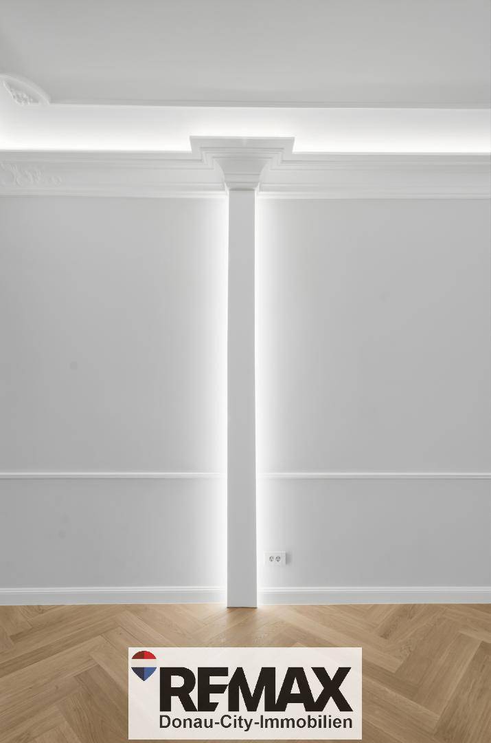 Wand mit klassischer Vertäfelung und einer beleuchteten Säule, die den Raum strukturiert.