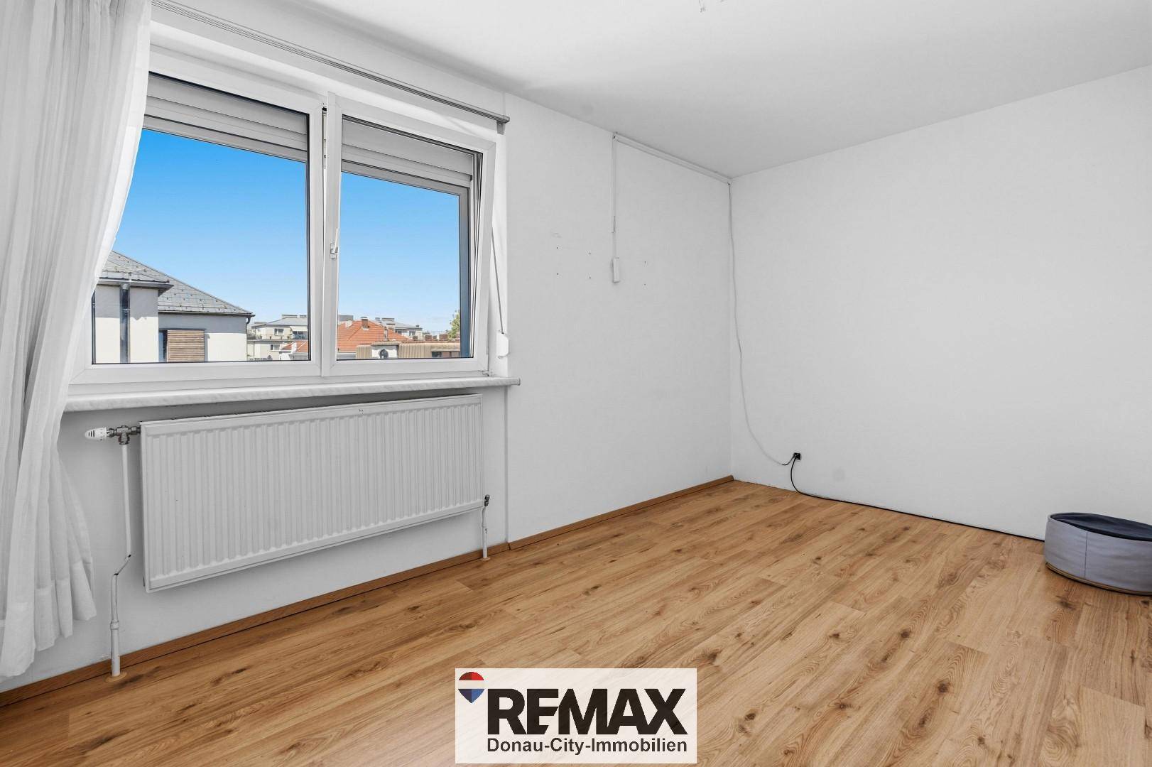 Helles Schlafzimmer mit Laminatboden und großem Fenster, bietet viel Tageslicht und Ausblick.