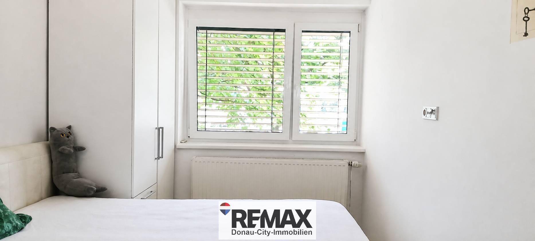 Helles Schlafzimmer mit Bett, weißem Kleiderschrank und Fenster mit Jalousien.