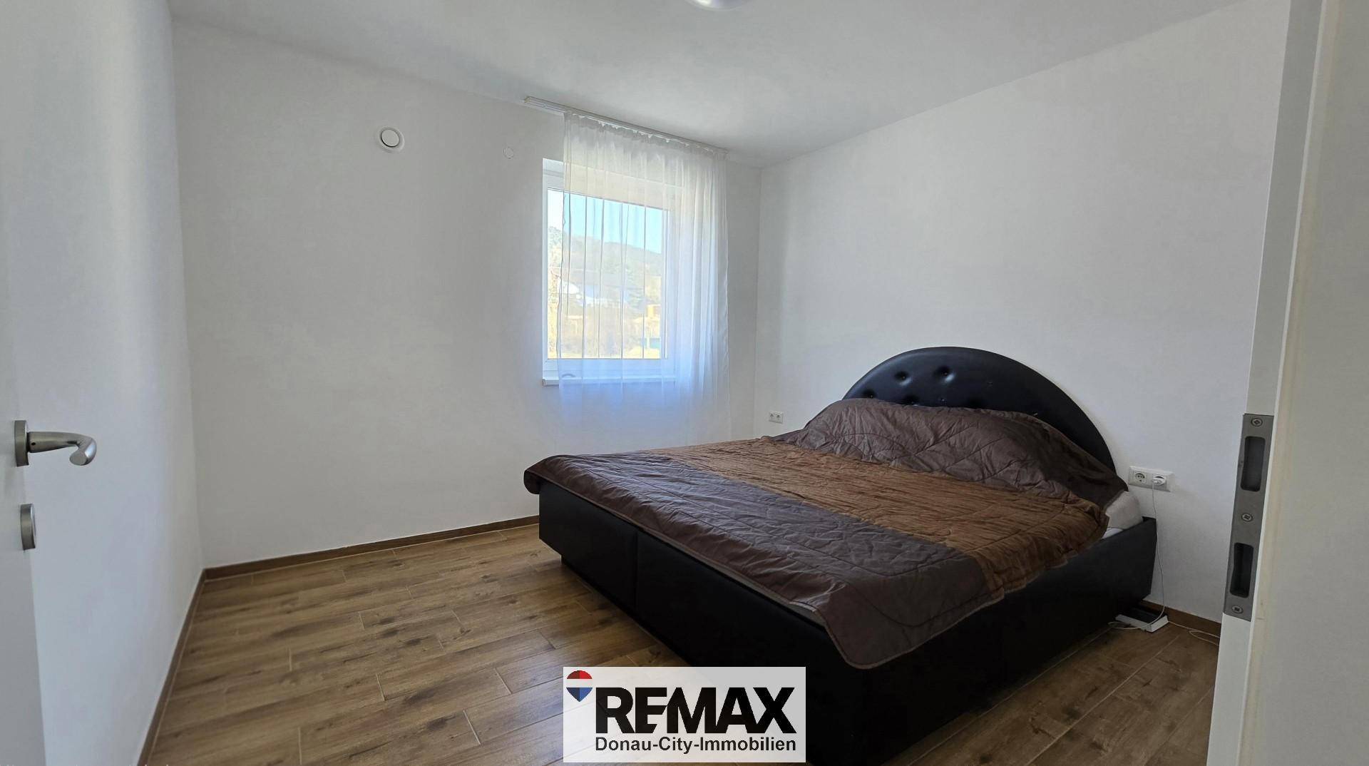 Schlafzimmer mit dunklem Bettrahmen, Holzboden und einem Fenster, das Tageslicht hereinlässt.