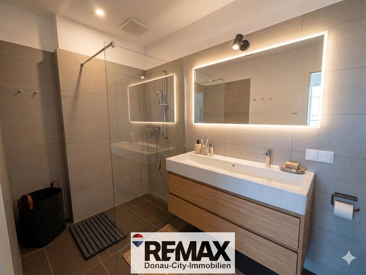 Modernes Badezimmer mit großer begehbarer Dusche, Holzwaschtisch und beleuchtetem Spiegel.