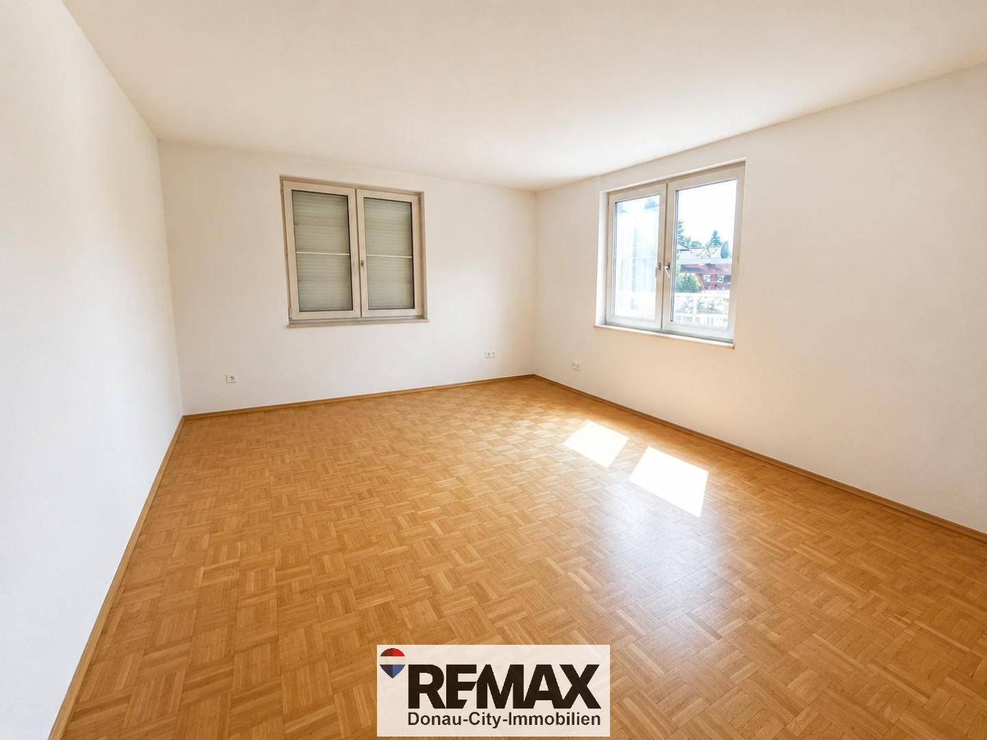 Geräumiges Zimmer mit hellem Parkettboden und großen Fenstern, die den Raum lichtdurchfluten.
