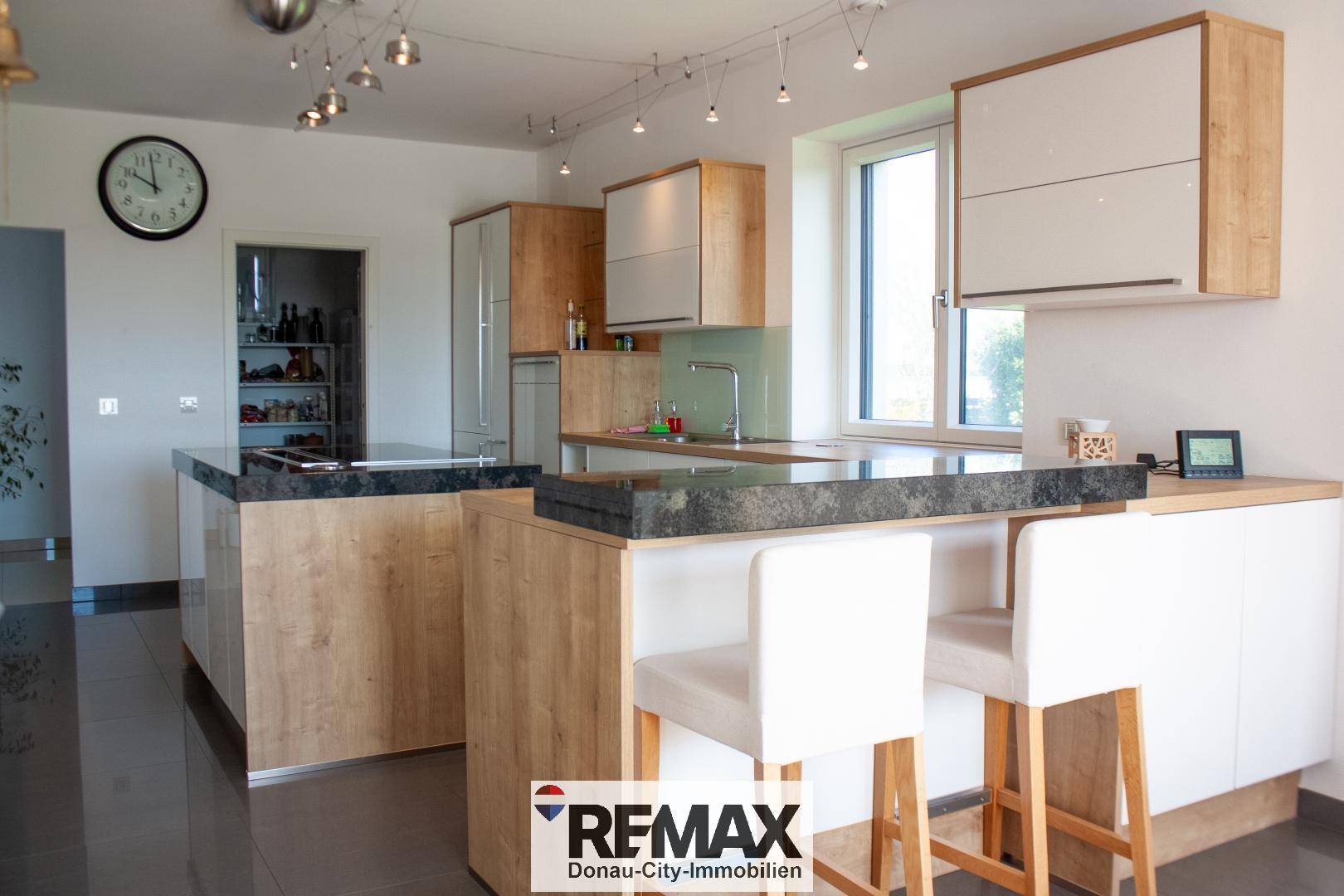 Moderne Küche mit Kücheninsel, Frühstücksbar und dunklen Arbeitsplatten, inklusive Speisekammer.