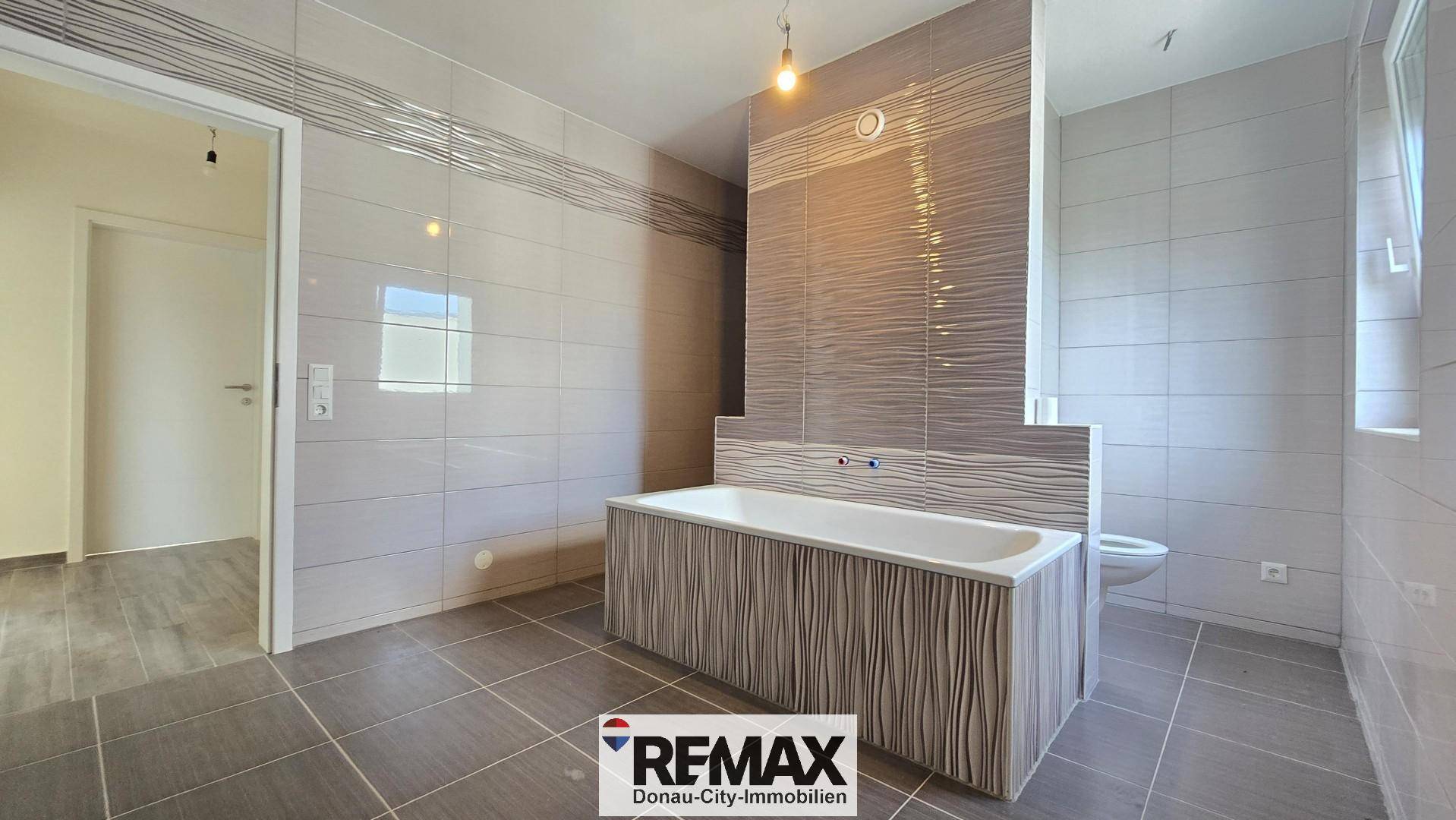 Modernes Badezimmer mit Badewanne und eleganten grauen Fliesen an Wänden und Boden.