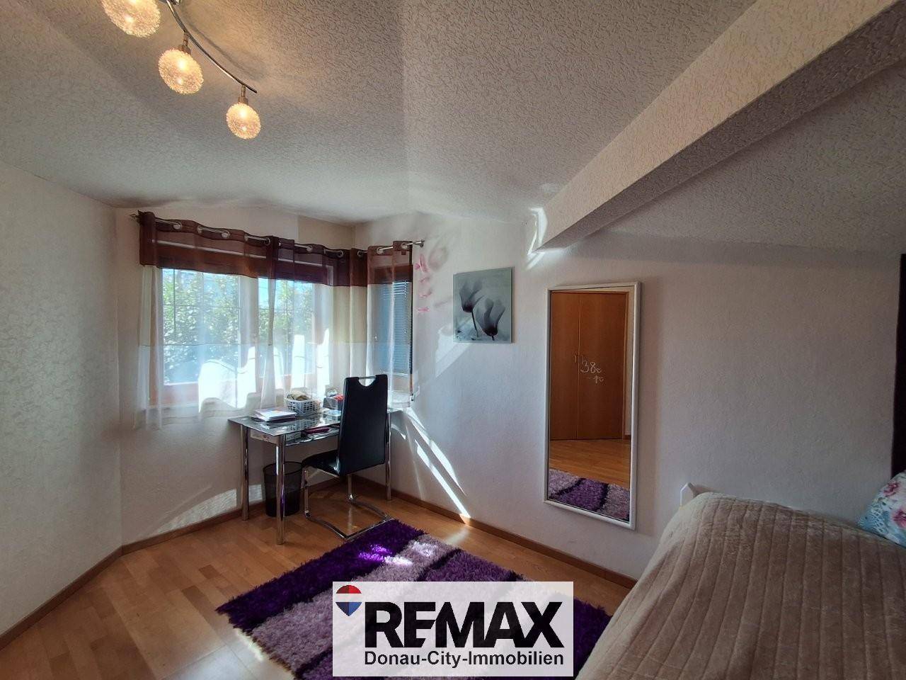 Helles Arbeitszimmer mit Schreibtisch, Stuhl und großem Fenster, ideal für Home-Office.