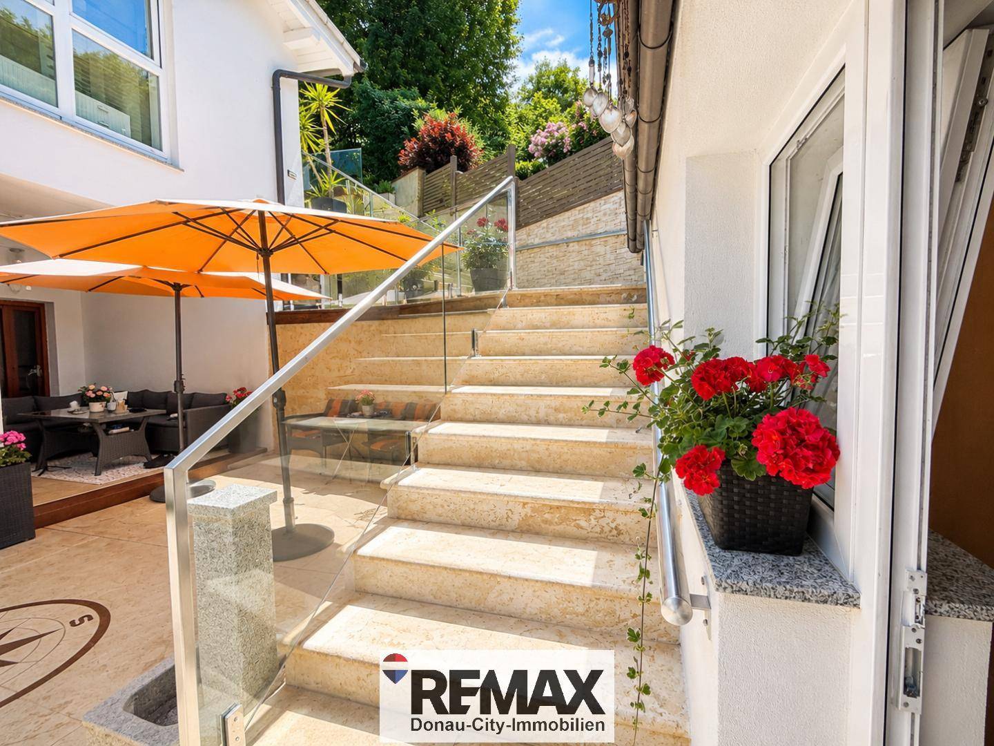 Elegante Außentreppe mit Glasgeländer und Blumenkästen führt zur oberen Ebene.