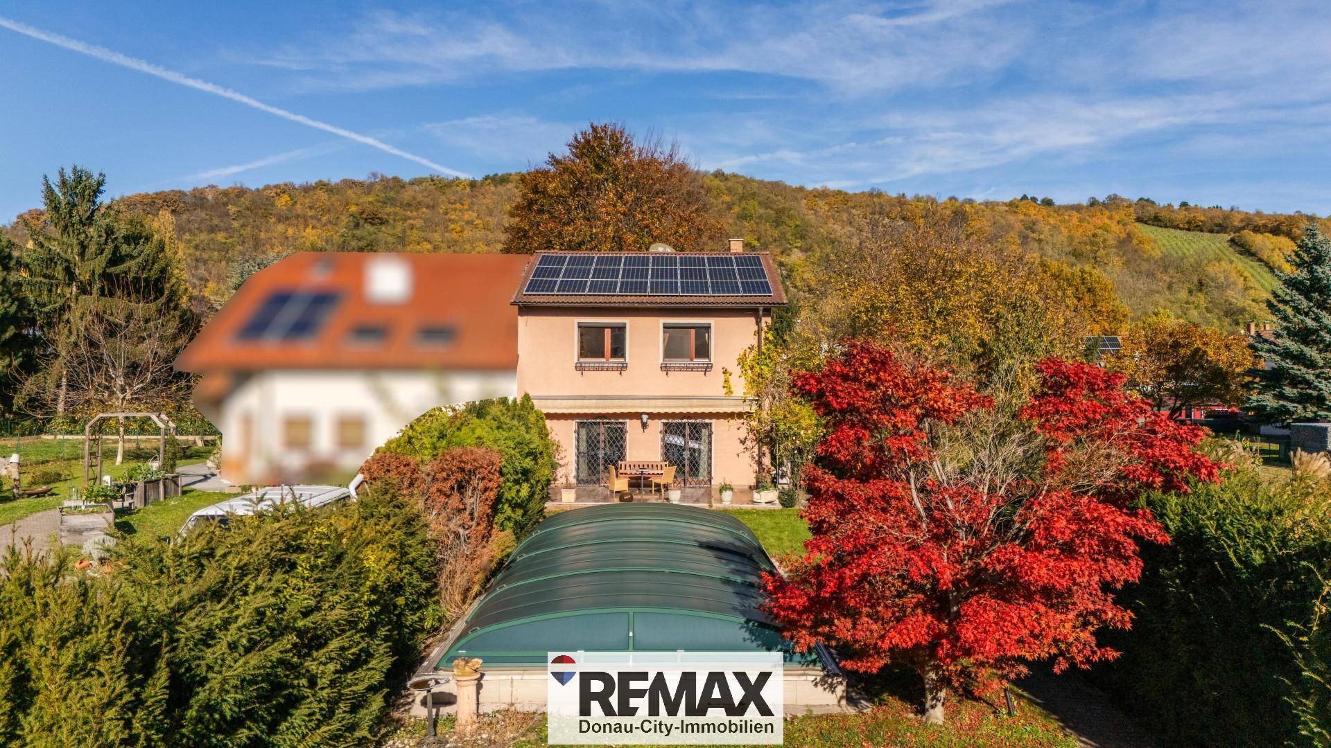 Hausfassade mit Solaranlage auf dem Dach, umgeben von einem gepflegten Garten mit Poolabdeckung.