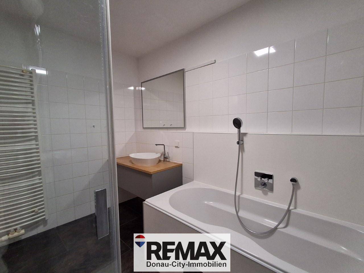 Modernes Badezimmer mit weißen Fliesen, Badewanne, Dusche, Waschbecken und Handtuchheizkörper.