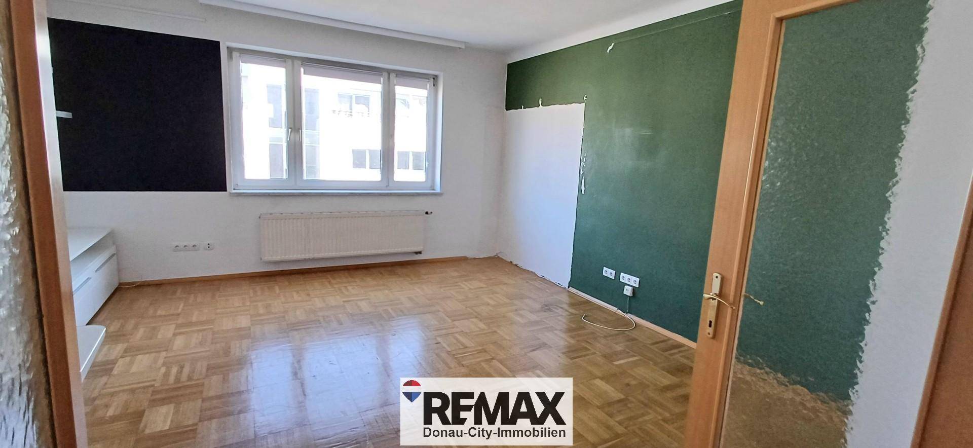 Geräumiger Raum mit Parkettboden und einer auffälligen grünen Wand, bereit zur Renovierung.