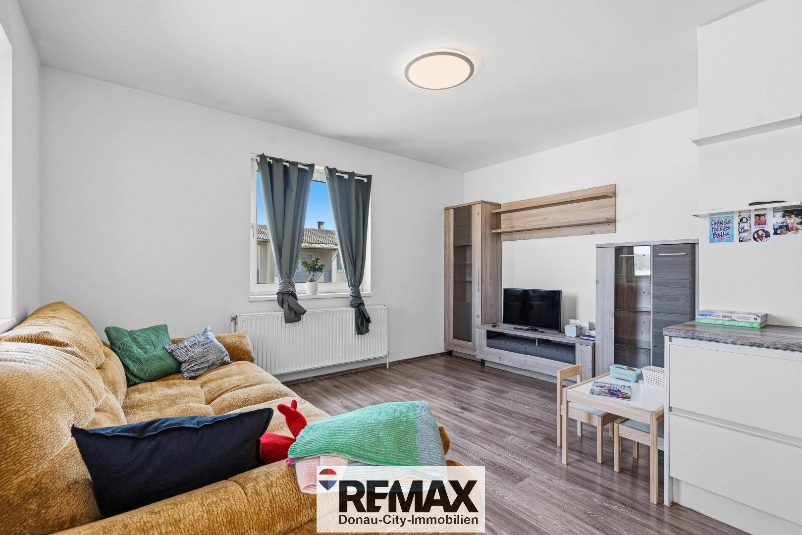 Gemütliches Wohnzimmer mit beiger Couch, TV-Möbeln und Laminatboden.