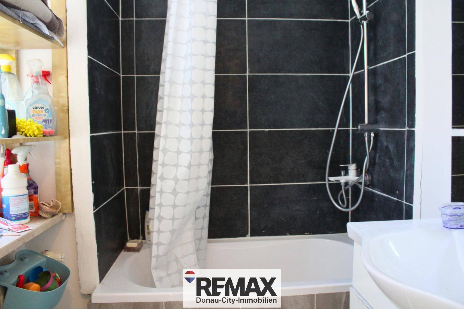 Badezimmer mit Badewanne, Duschvorhang und schwarzen Fliesen an den Wänden.