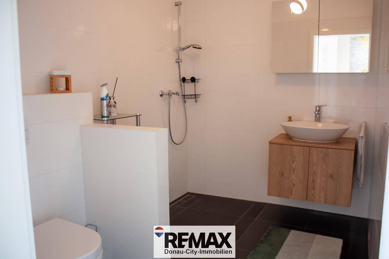 Modernes Badezimmer mit ebenerdiger Dusche, wandhängendem WC und stilvollem Waschbecken.